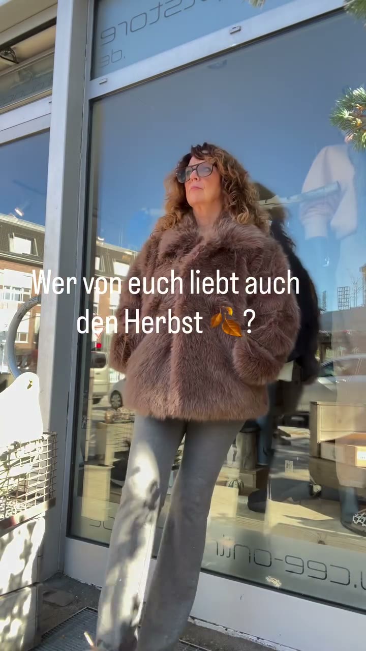 CEE in einer taupe-braunen Jacke in Pelzoptik über grauem Homewear-Outfit vor dem Schaufenster des CEE! Conceptstore.