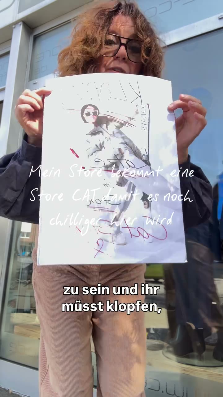 CEE hält vor dem CEE! Conceptstore ein selbst gestaltetes Schild mit der Aufschrift Klopfen hoch, weil der Store eine Katze bekommt.